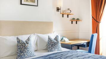 Ein Hotelzimmer mit einem Bett, einem Schreibtisch, einem Stuhl, einem Telefon und einem an der Wand befestigten Regal mit Lampe und Tasse.