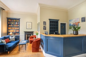 A well-furnished living room with a blue sofa, a fireplace, a bookshelf, and a reception desk.
