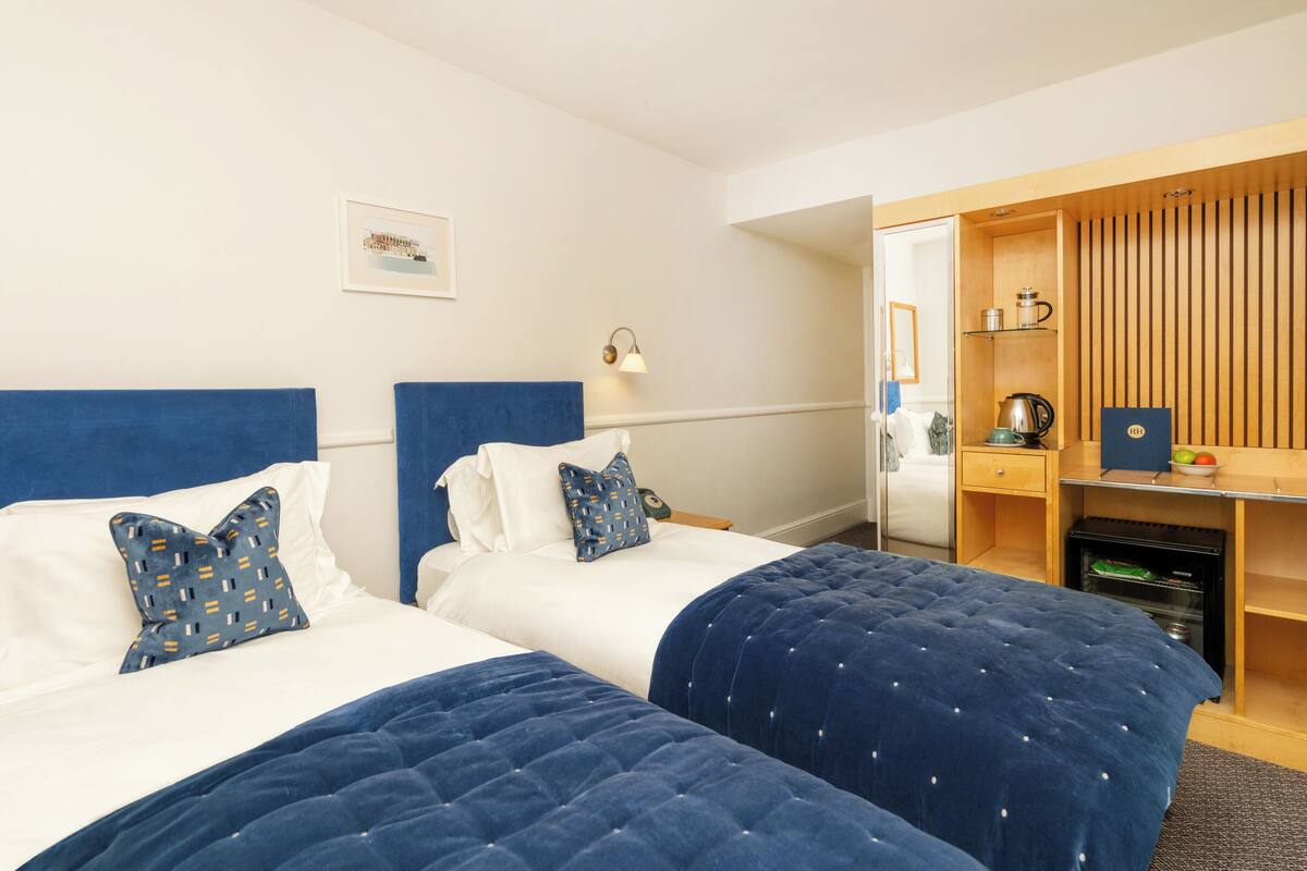 A hotel room with two beds, a desk, a wardrobe, and a small kitchenette.