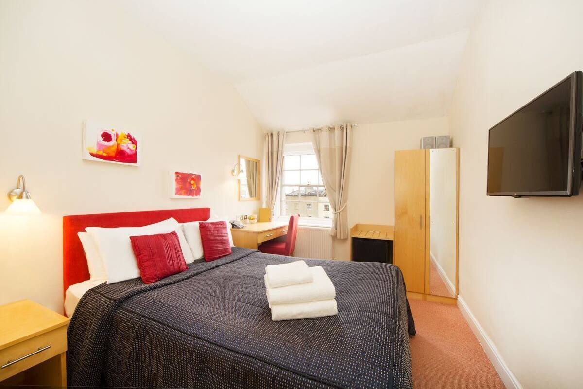 A hotel room with a bed, a desk, a chair, a TV, and artwork on the walls.