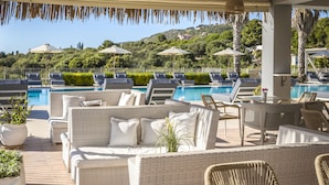 Zona de piscina con sillones de descanso y un área de estar cubierta con vistas a una piscina y una colina.