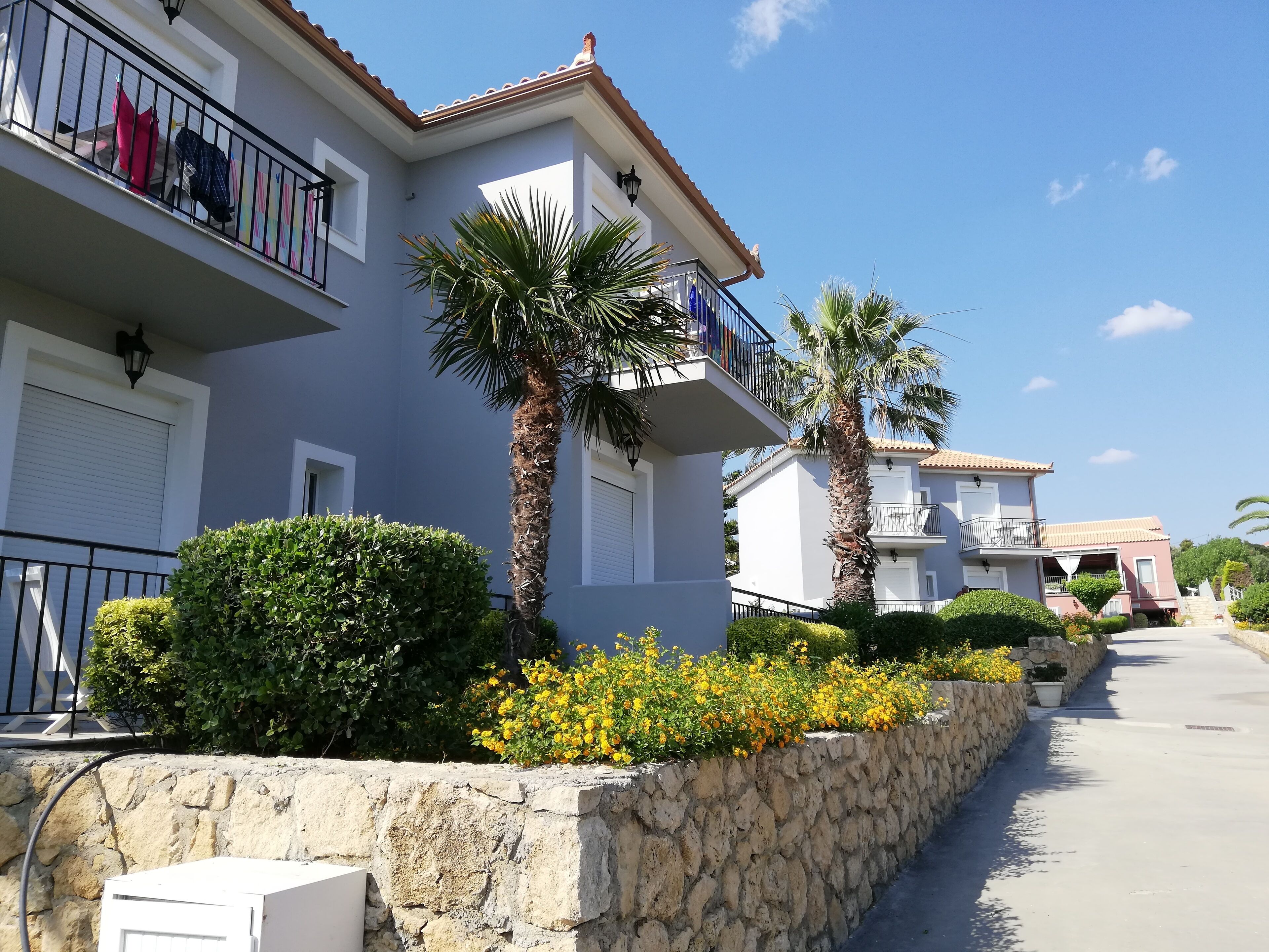 A residential building with balconies, stone walls, and palm trees.