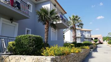 A residential building with balconies, stone walls, and palm trees.