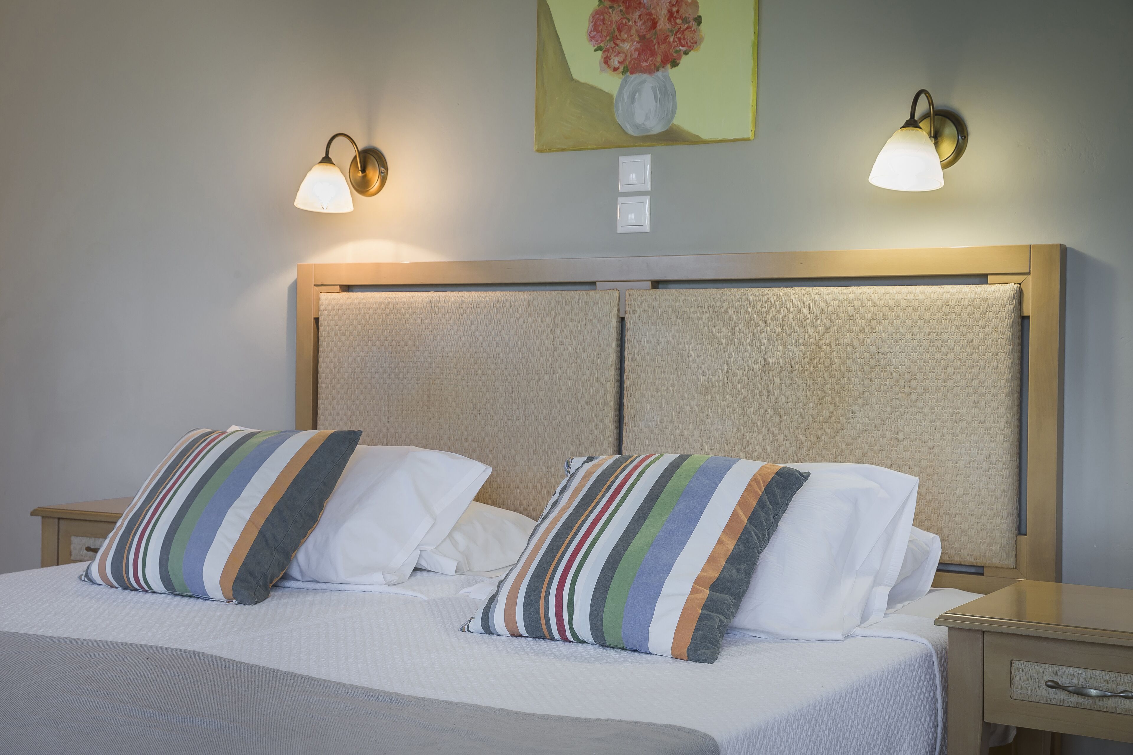 A double bed with striped pillows, a headboard with a textured panel, and two wall-mounted lamps.