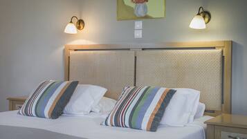 A double bed with striped pillows, a headboard with a textured panel, and two wall-mounted lamps.