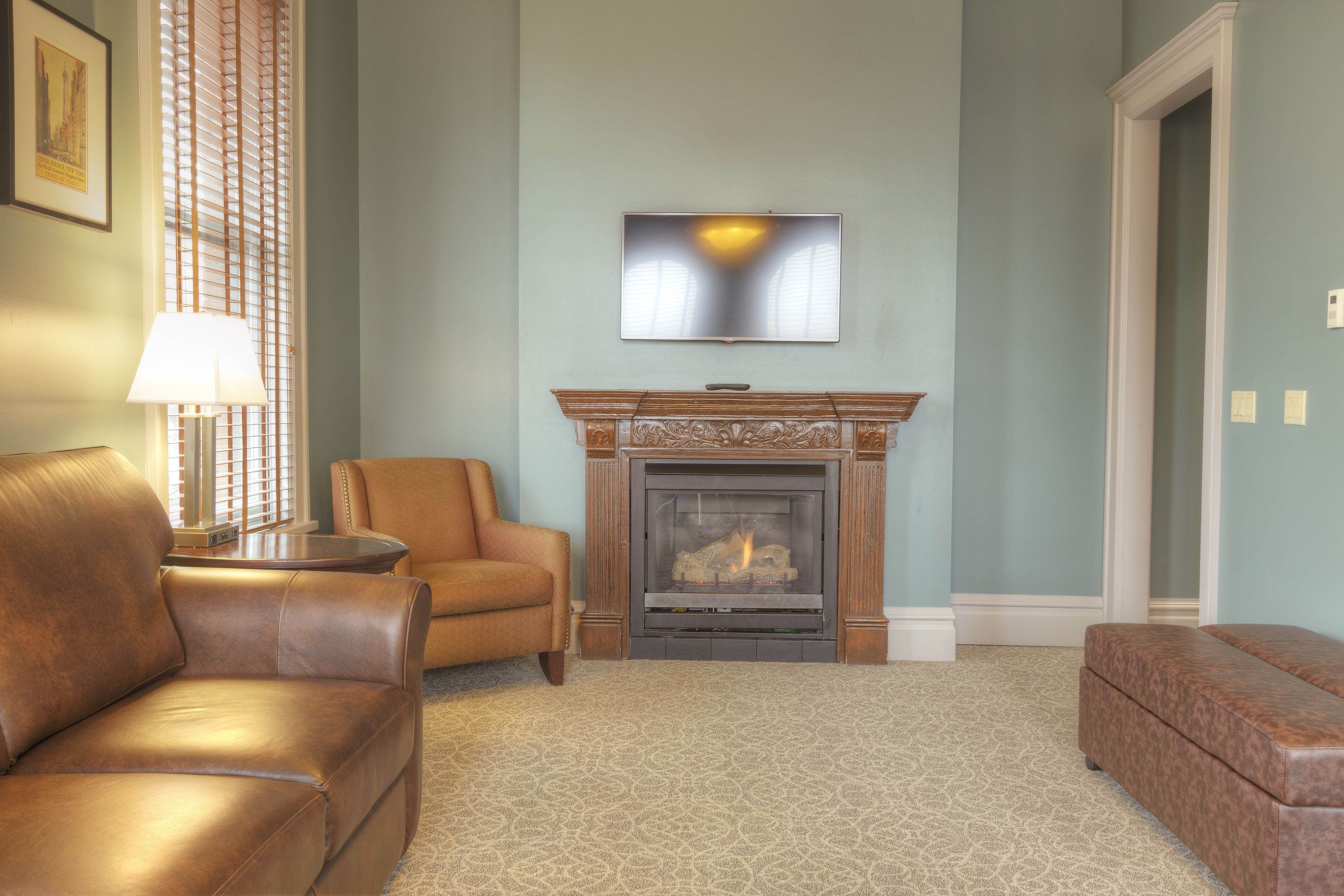 A living room with a fireplace, a sofa, a chair, and a television mounted on the wall.