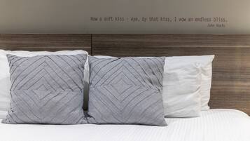 Una cama con dos almohadones estampados y una almohada lisa, un cabecero de madera y una cita en la pared.