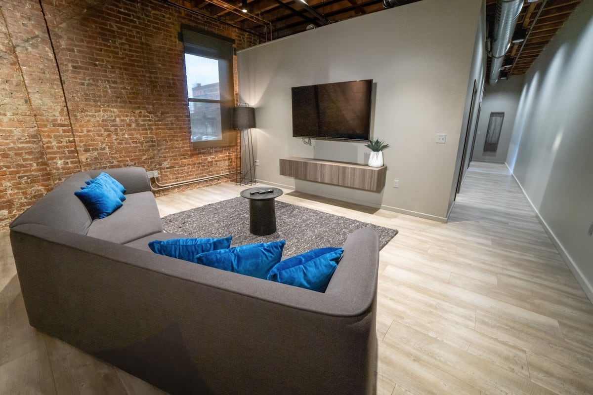 A modern living room with a gray sectional sofa, a coffee table, and a flat-screen TV mounted on a wall.