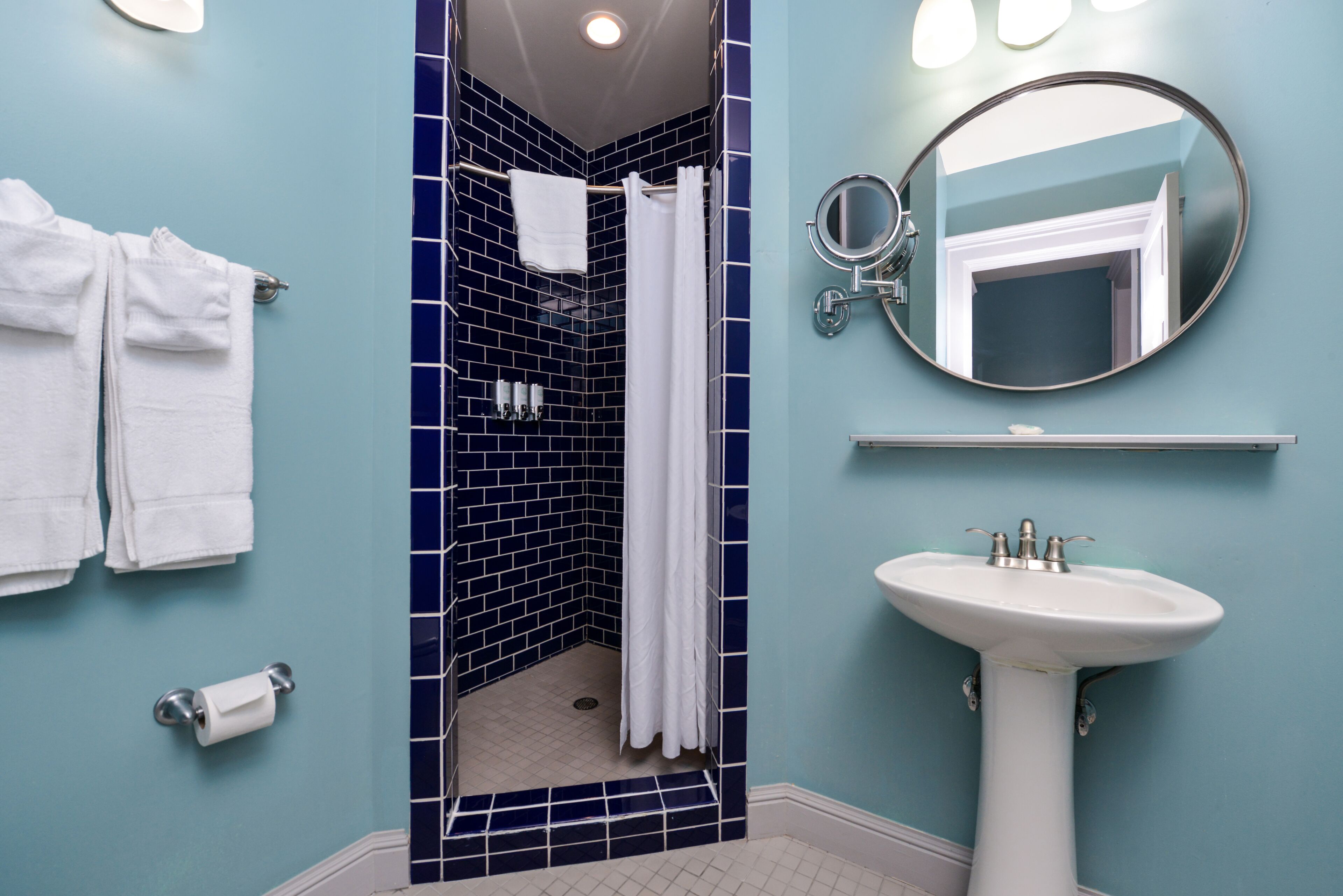 A bathroom with a blue tiled shower, a white sink, and a mirror.