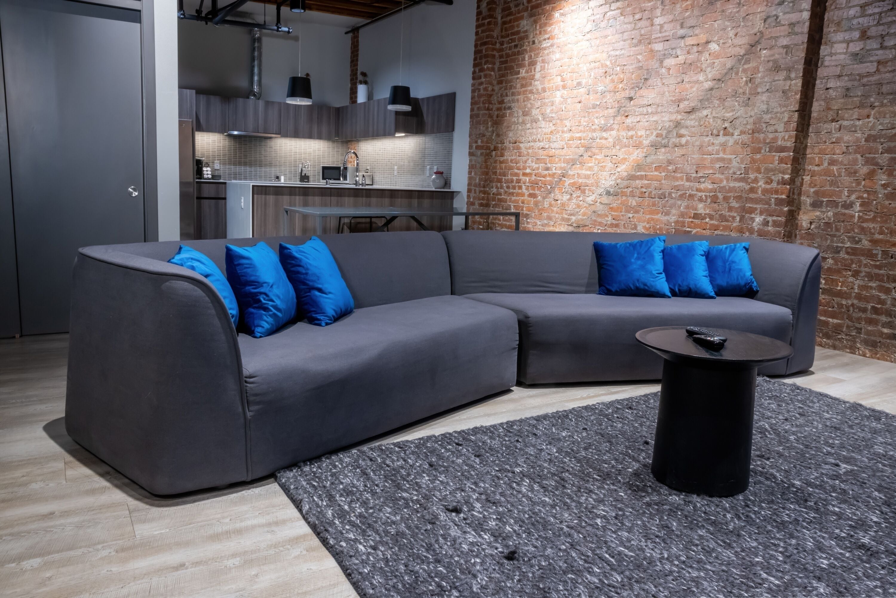 Uma sala de estar moderna com um sofá seccional cinza, almofadas azuis e uma mesa de centro preta.
