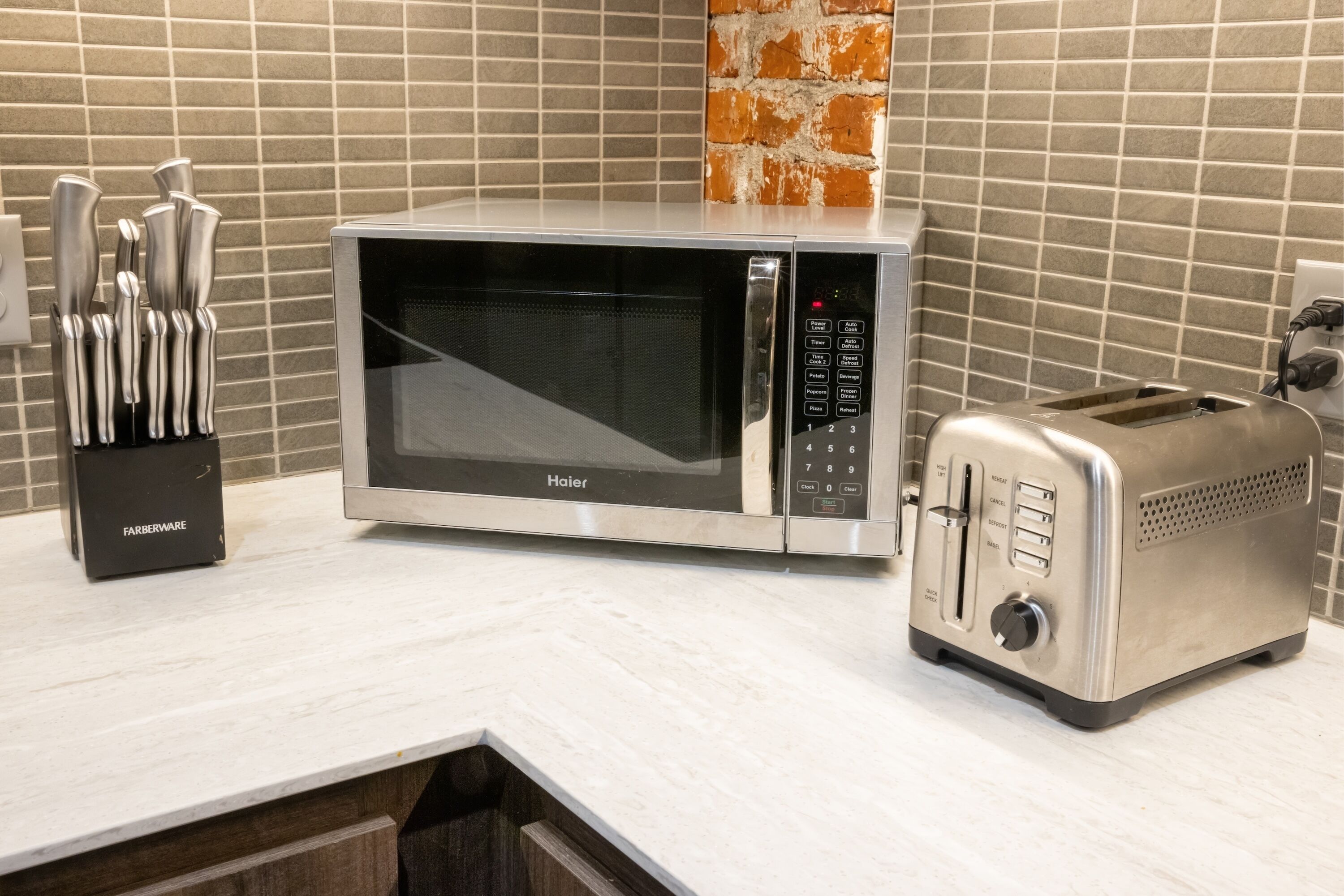 A kitchen with a microwave and toaster on the counter, a knife block, and a brick wall backsplash.