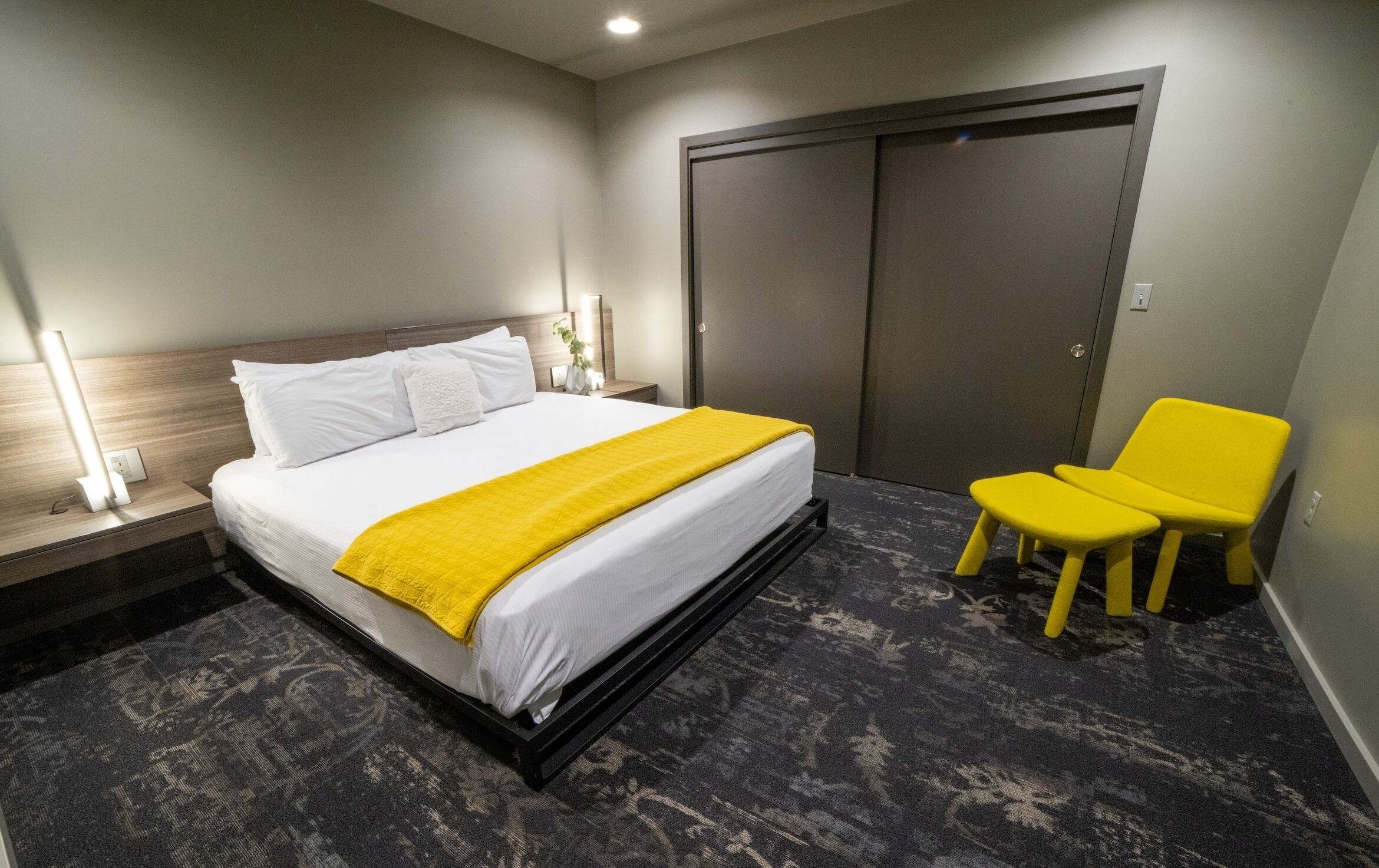 A hotel room with a bed, a nightstand, a lamp, a chair, and a wardrobe.