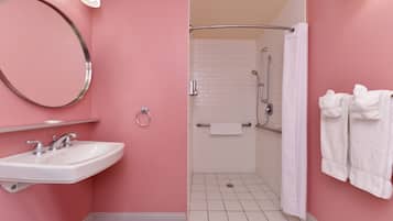 Un baño con pared rosa, azulejos blancos, un lavamanos con espejo, una ducha con cortina y toallas en la pared.