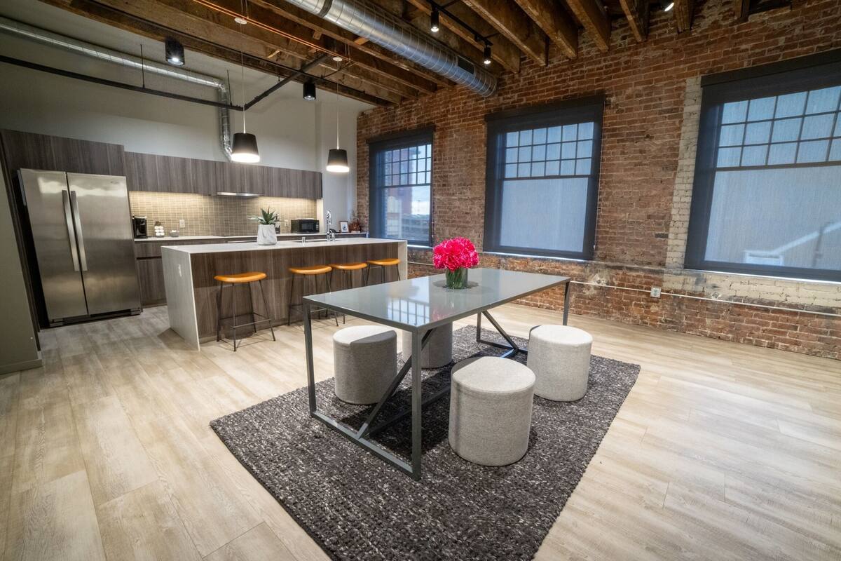 A modern kitchen with a central island, bar stools, and a dining table with stools.