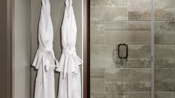 A bathroom with two white towels hanging on hooks, a shower area with a glass door, and a tiled wall.