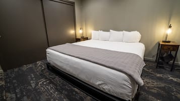 Habitación de hotel con una cama grande, dos mesitas de noche con lámparas, un armario y suelo alfombrado.