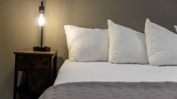 Una cama bien hecha con almohadas blancas y una colcha estampada, una mesita de noche con lámpara y una silla.