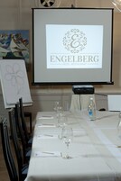 Mesa de conferência com tela de projetor exibindo o logotipo do Restaurante Hotel Engelberg, quadro branco com um desenho de flor e uma garrafa de água na mesa.