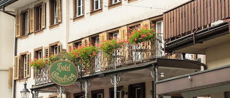 Un hotel con balcón decorado con flores, mobiliario exterior y un letrero.