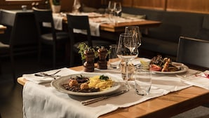 A dining table set with plates of food, wine glasses, and cutlery. - Hotel Engelberg das Trail Hotel (Engelberg)