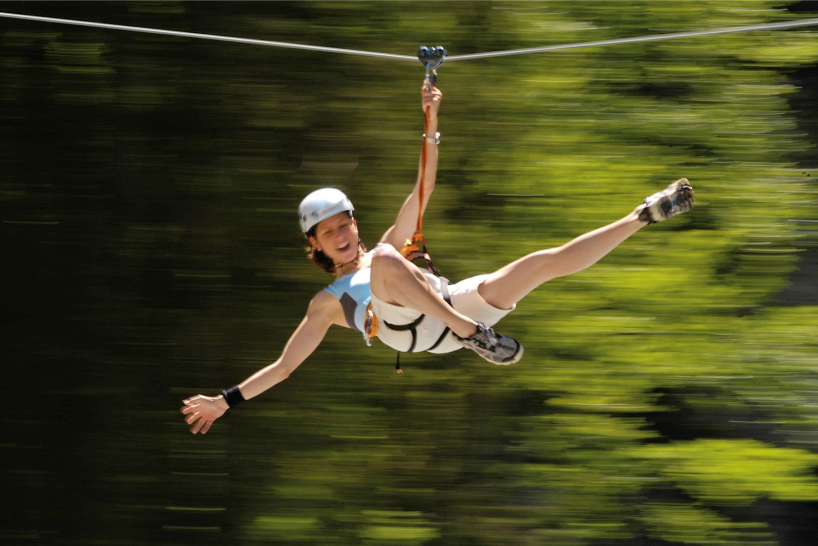 A person in a white outfit and helmet, suspended in mid-air by a zip line.
