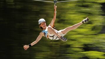 A person in a white outfit and helmet, suspended in mid-air by a zip line.