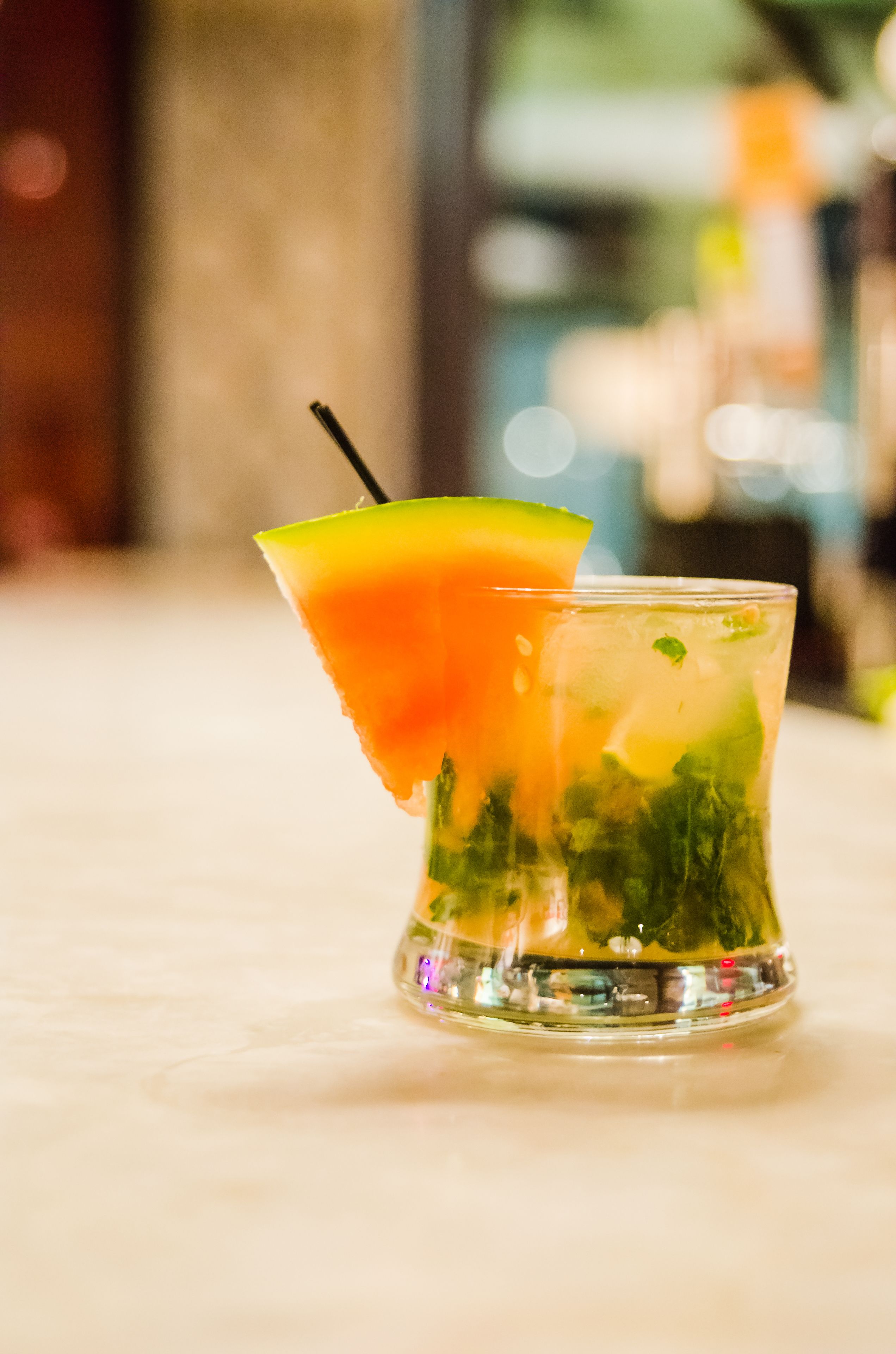 En cocktail med en limeskiva och ett sugrör, serverad i ett glas med is och örter.
