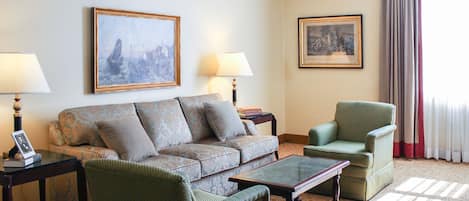 A living room with a sofa, armchairs, a coffee table, lamps, and framed pictures on the walls.