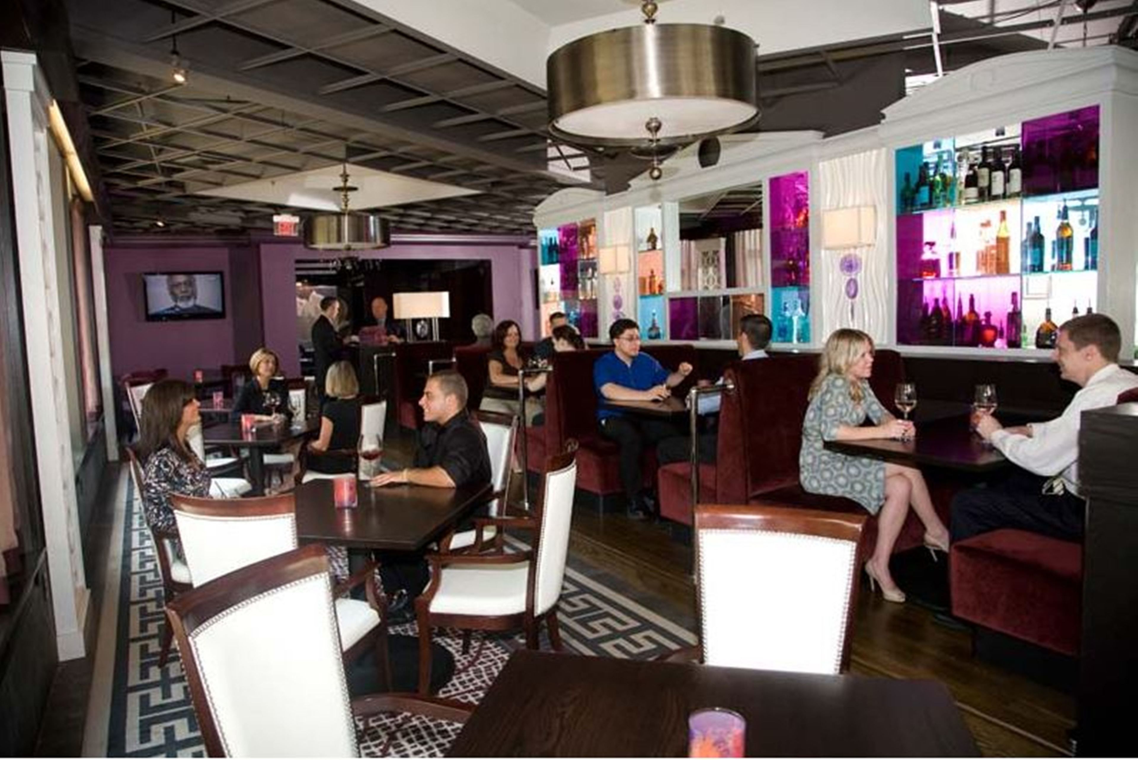 A restaurant with tables and chairs, a bar area with bottles, and a television screen.