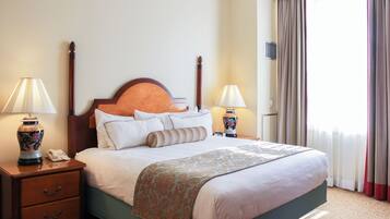 Una habitación de hotel con una cama, dos mesitas de noche con lámparas, una mesita de noche con teléfono y una ventana con cortinas.
