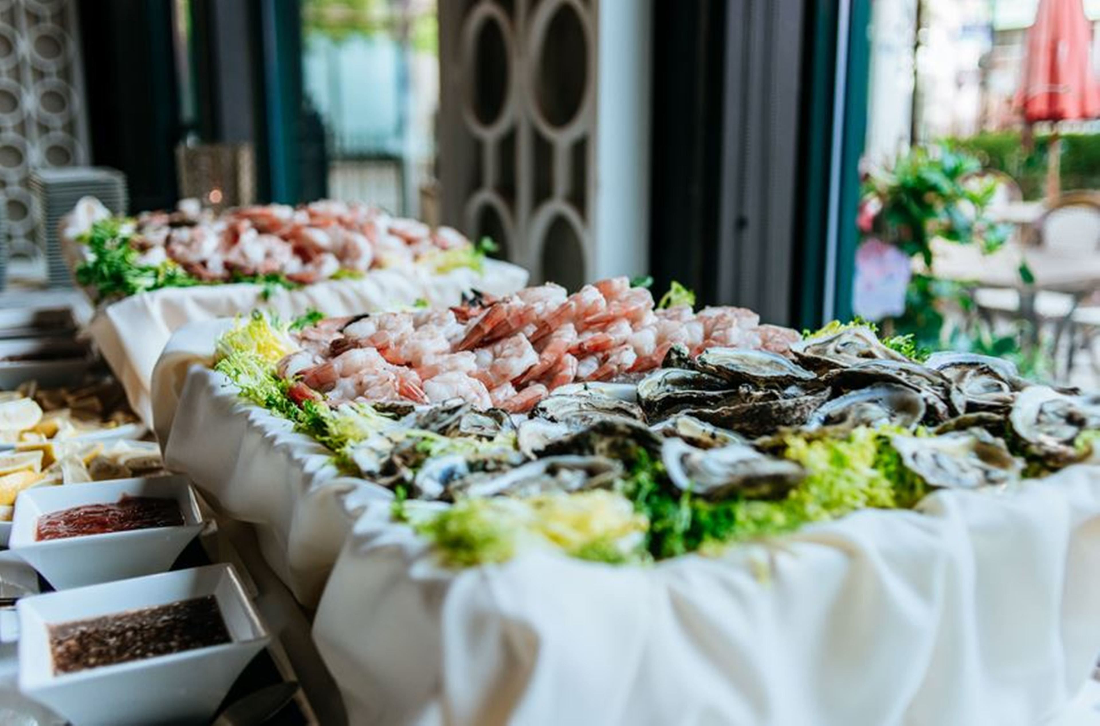 Un tavolo per buffet con diverse opzioni di pesce, tra cui gamberi e ostriche, disposte su una tovaglia con bordo decorativo.