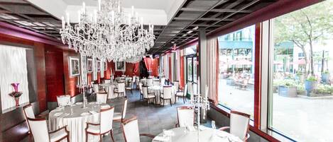 A restaurant with round tables, white chairs, and a large chandelier.