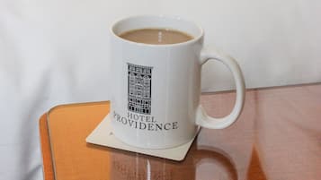 Eine weiße Tasse mit Hotel-Logo auf einem Untersetzer, platziert auf einem Holznachttisch in einem Hotelzimmer.