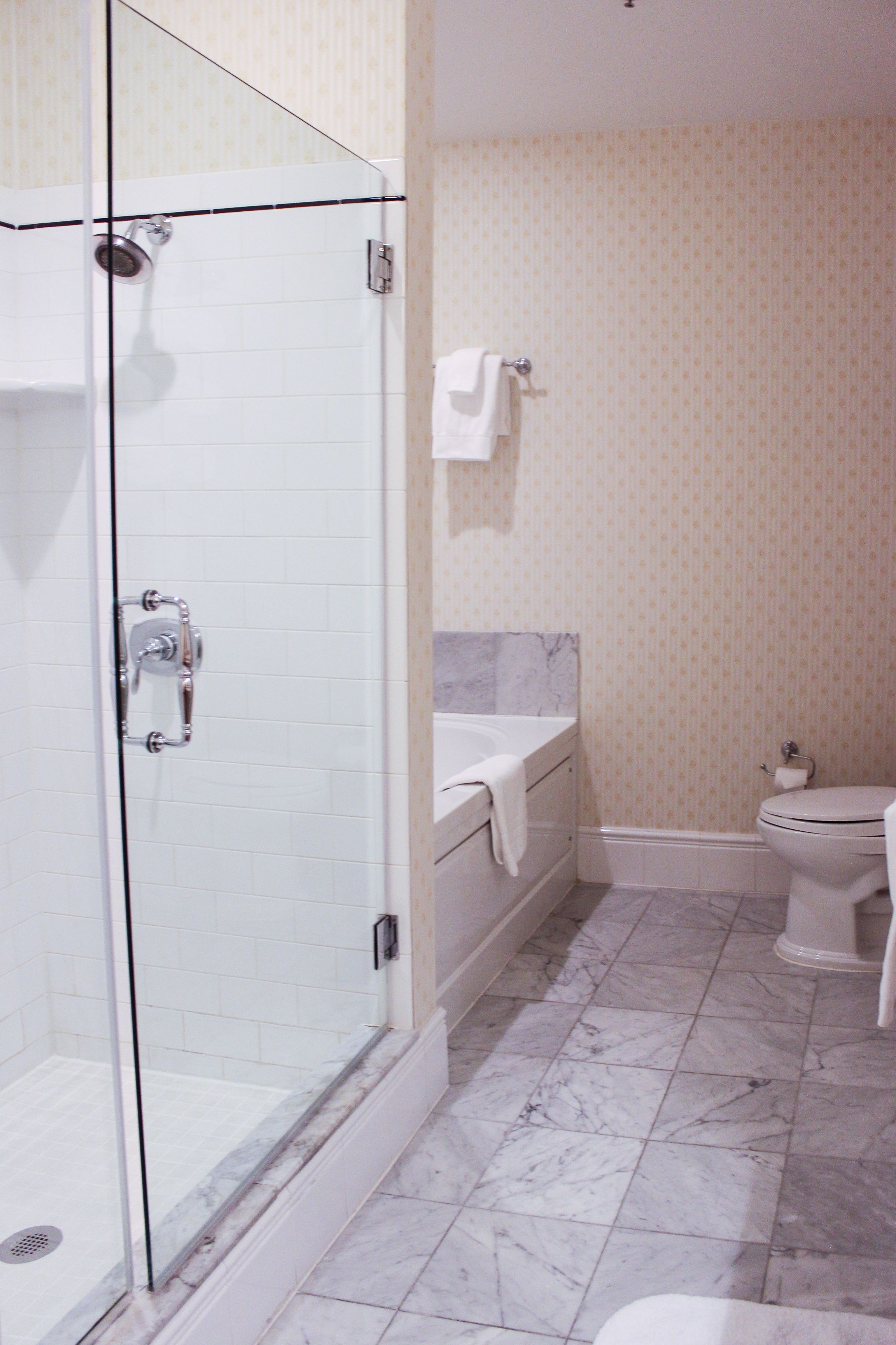 A bathroom with a glass shower enclosure, a bathtub, a toilet, and a marble-tiled floor.