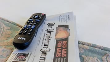 A bed with a striped pillow, a remote control, and a newspaper on a patterned blanket.
