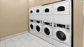 Une rangée de lave-linge et de sèche-linge blancs, modernes et fixés au mur, dans une buanderie propre et carrelée.