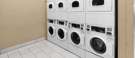 A row of white, modern, wall-mounted washers and dryers in a clean, tiled laundry room.
