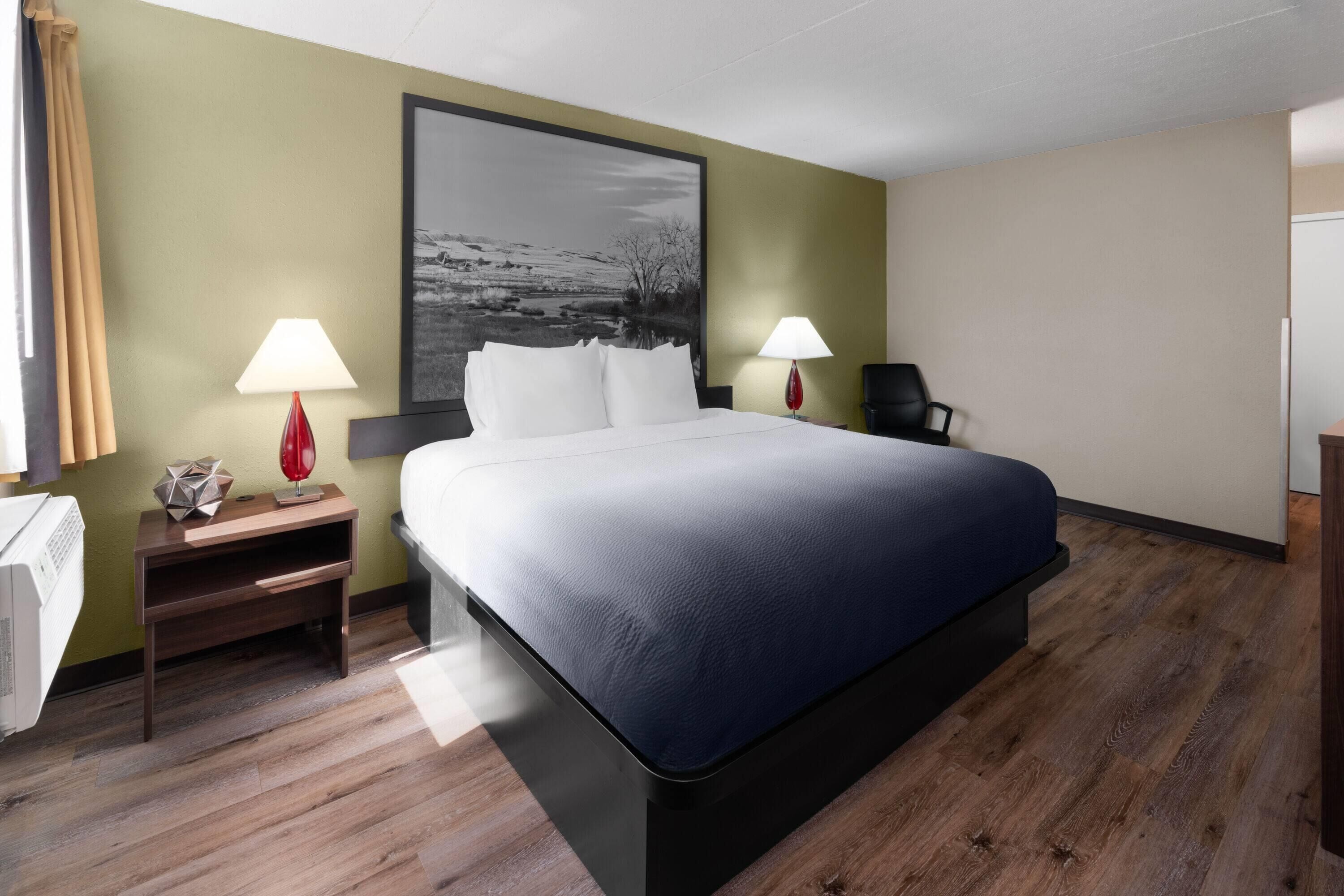 A hotel room with a large bed, two bedside tables with lamps, a chair, and a large framed picture on the wall.