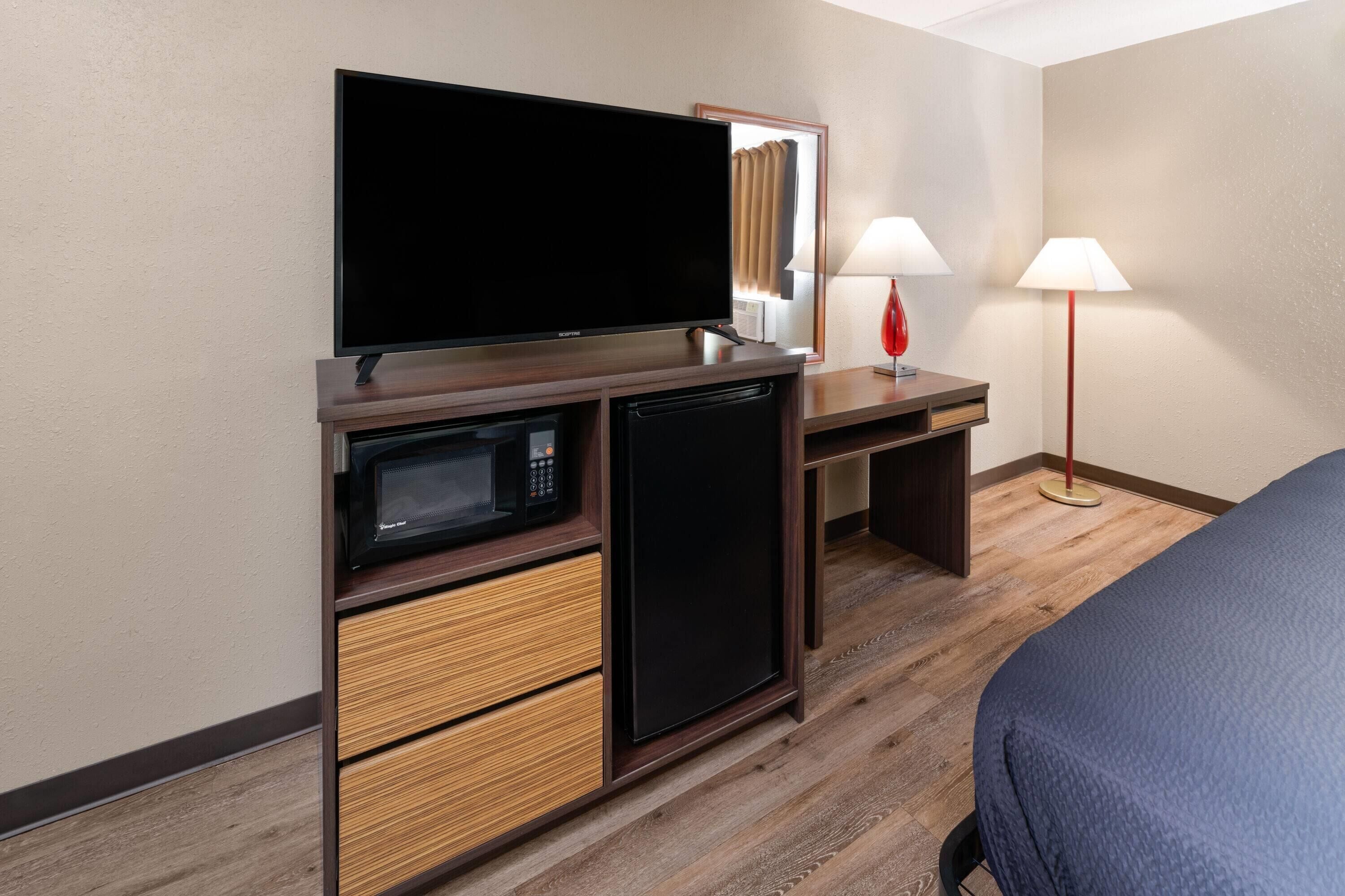 A hotel room with a bed, a TV, a microwave, a refrigerator, a desk, and two lamps.