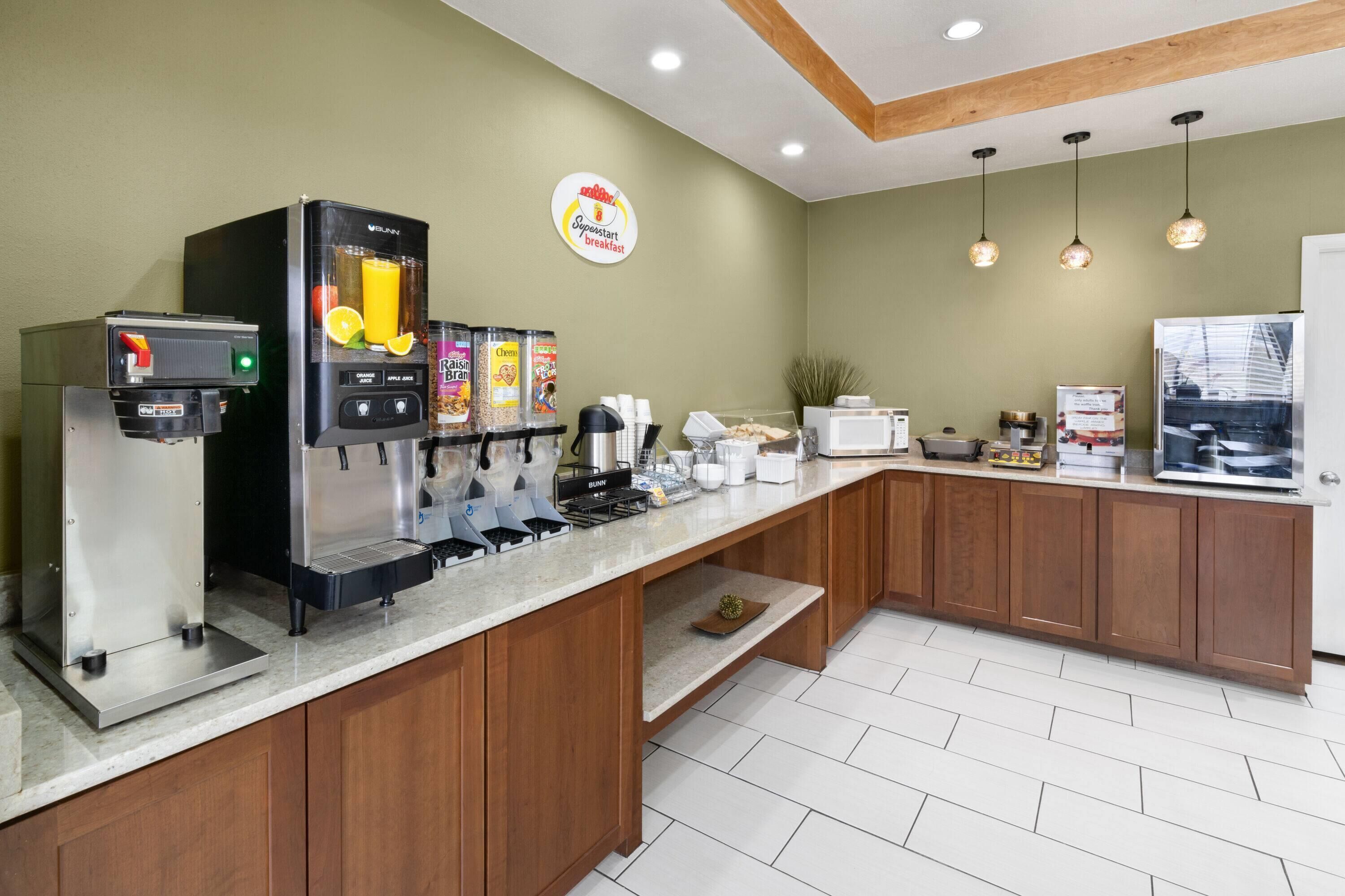 A breakfast bar with a coffee machine, juice dispenser, and various food items.