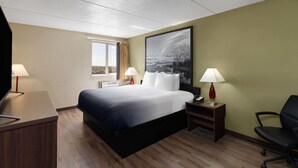 Une chambre d’hôtel comprenant un lit, deux tables de chevet, un bureau, une chaise, une télévision et une fenêtre avec des rideaux.
