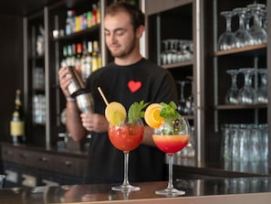 A bartender preparing cocktails with garnishes, behind a bar with shelves of bottles and glasses.