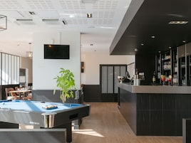 A modern bar area with a pool table, a bar counter, and a television mounted on the wall.