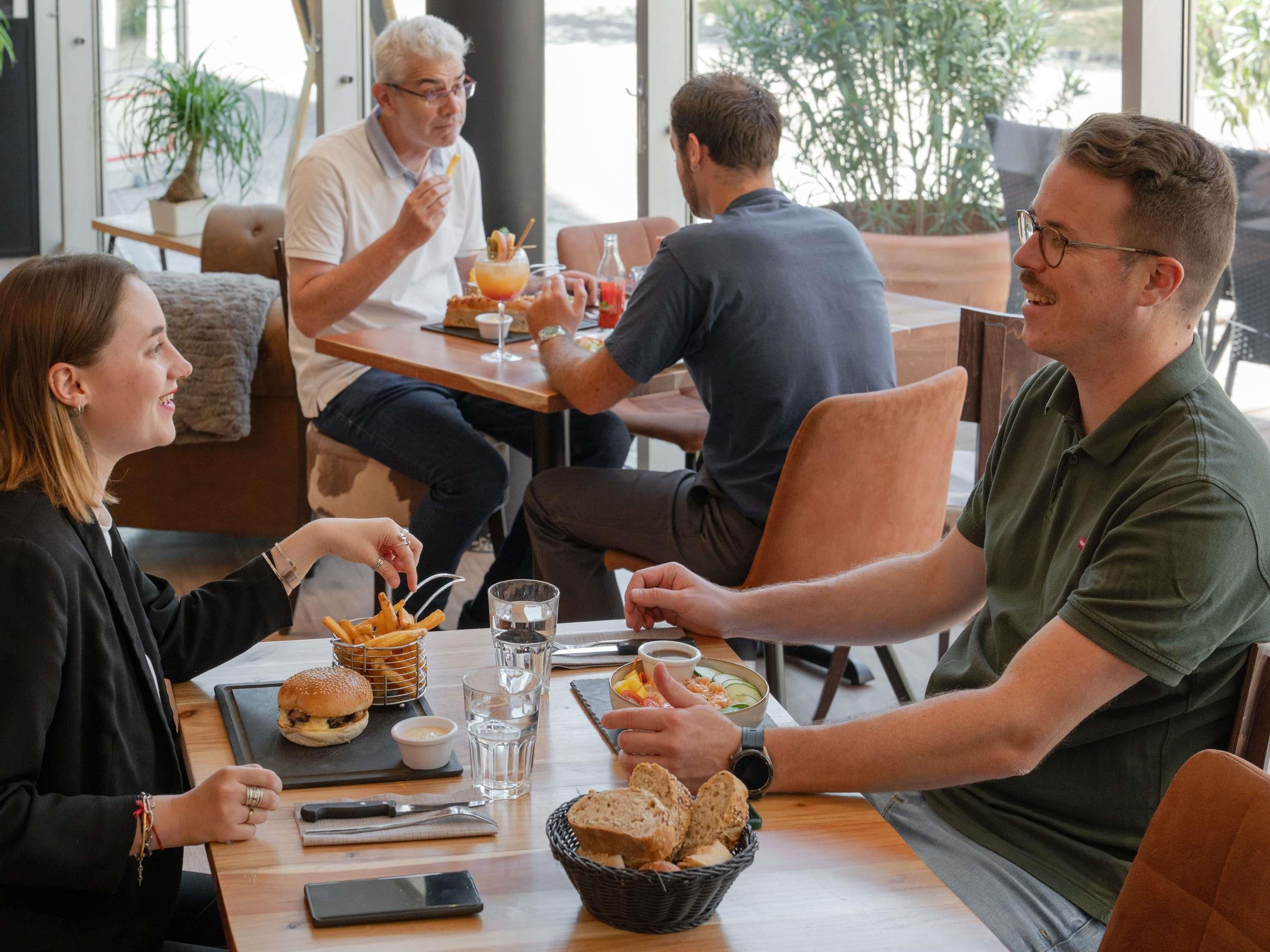 Un groupe de personnes est assis à une table, devant des plats, des boissons et un téléphone intelligent.