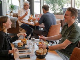 Un grupo de personas cenando en una mesa con comida, bebidas y un teléfono inteligente.