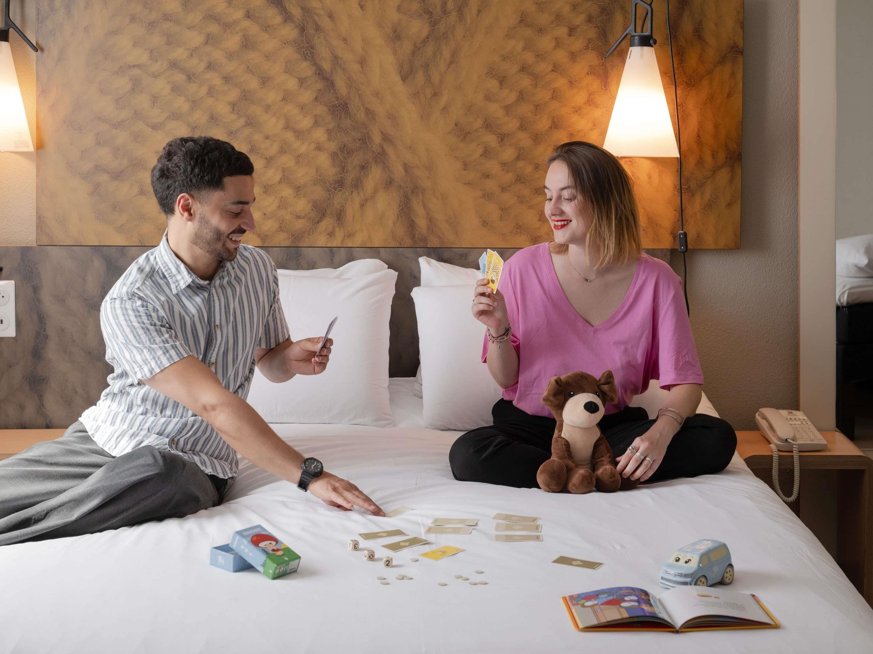 A hotel room with a bed, a lamp, a teddy bear, and a book.