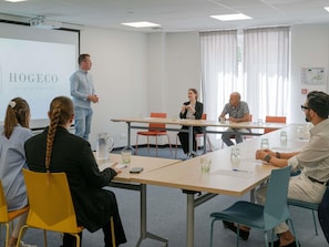 A conference room with a projector screen, a presentation, and attendees seated around a table.