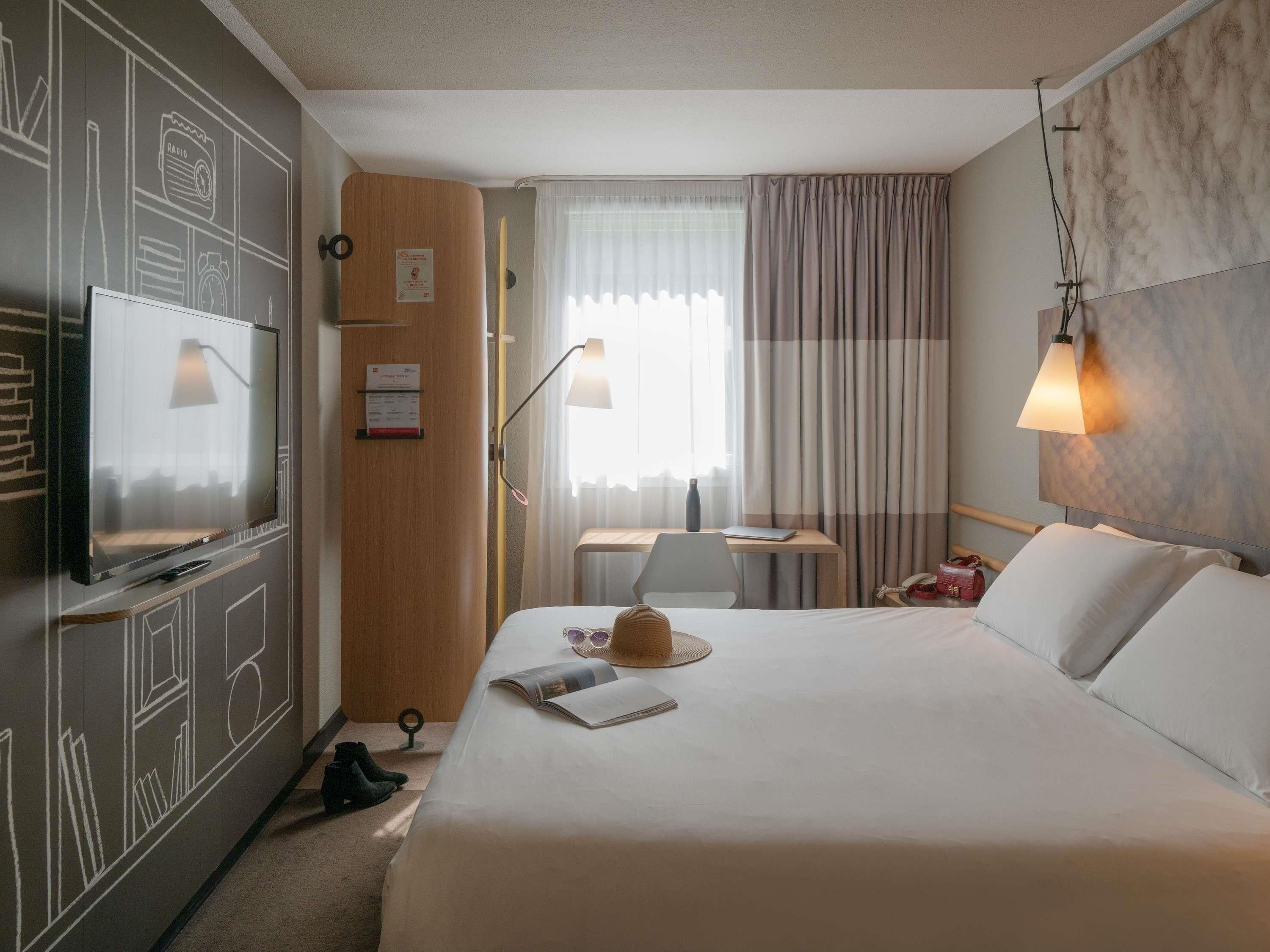 Habitación de hotel con cama, escritorio, televisor y una pared con diseño de pizarra.