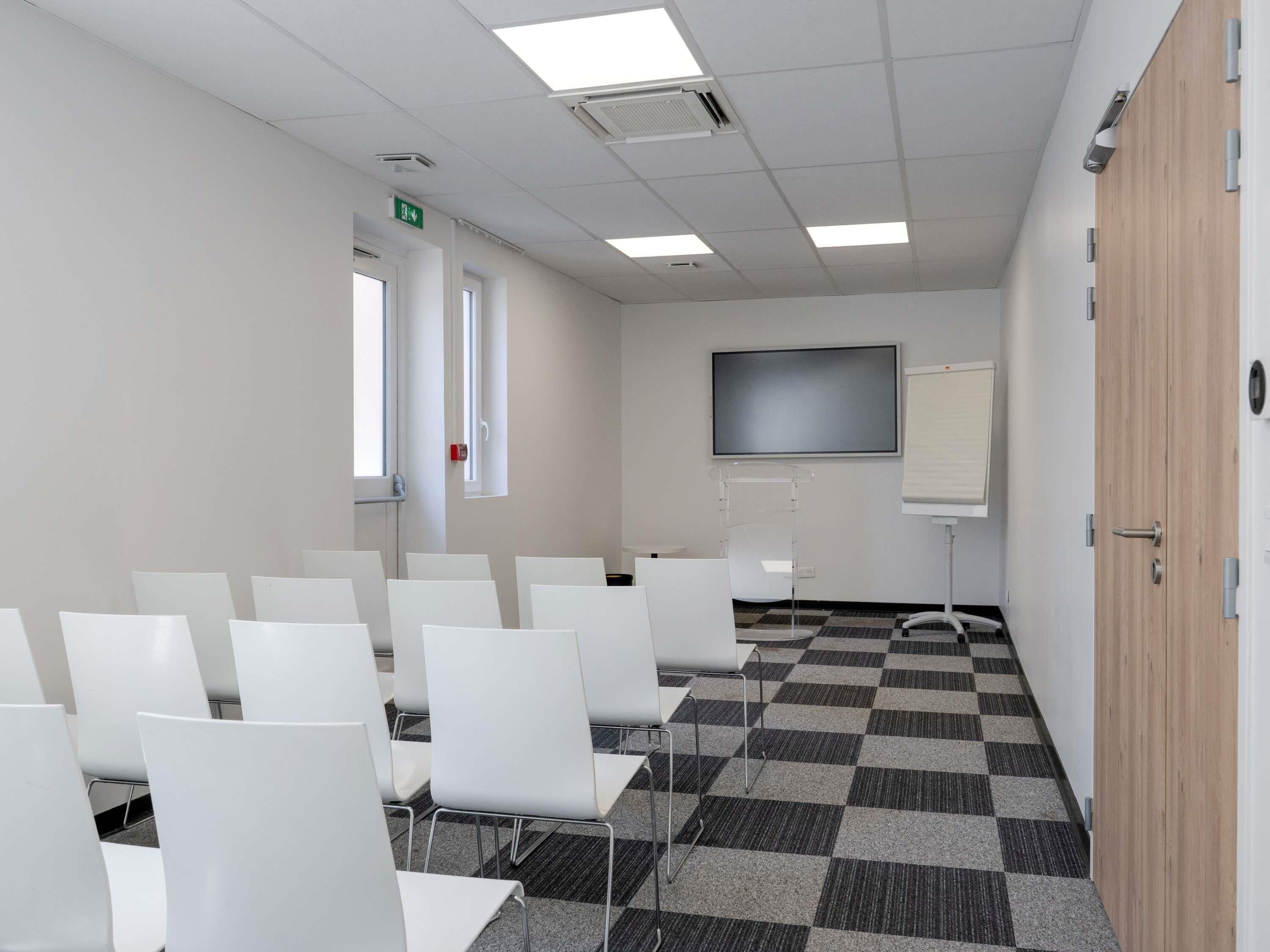 A conference room with white chairs, a large screen, and a checkered floor.
