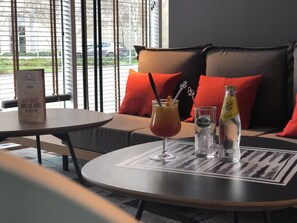 A cozy seating area with a table set for two, featuring a drink with a cocktail stirrer and a bottle of water. - ibis Lyon Caluire Cité Internationale (Caluire-et-Cuire)